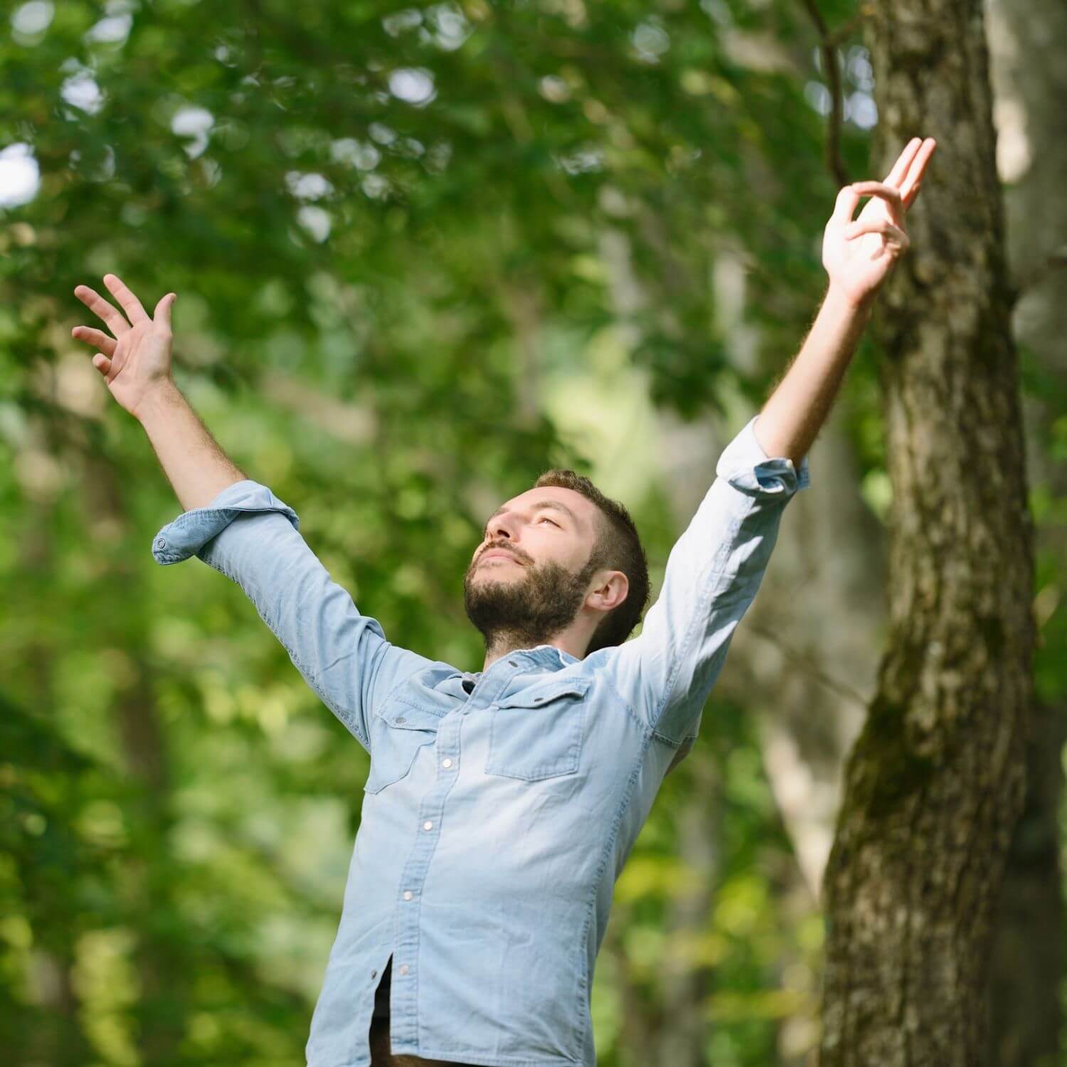Man with arms raised joyfully outdoors, celebrating nature and freedom in a lush green forest.