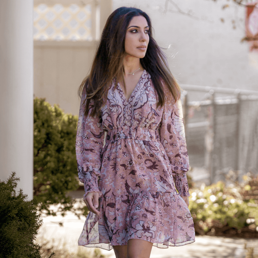 Model wearing a floral patterned dress, walking outdoors in a sunny setting.