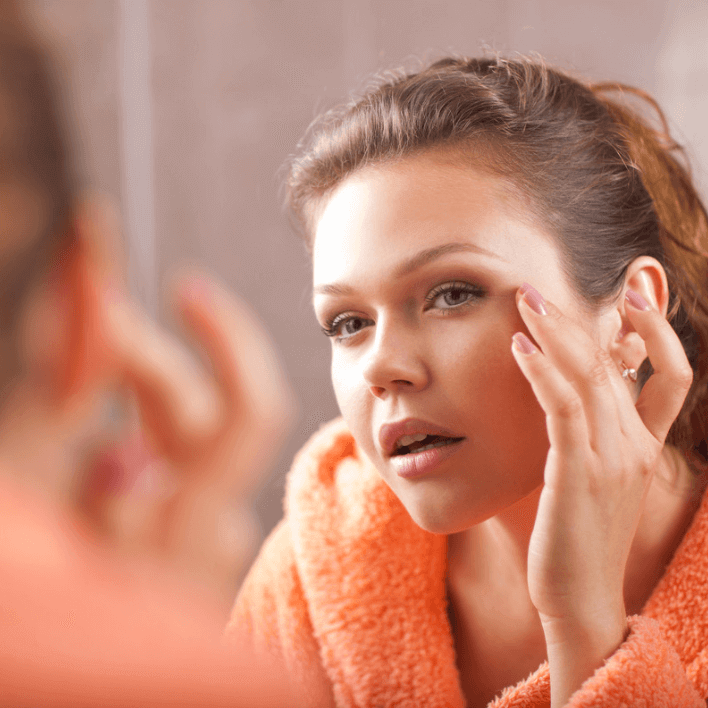 Woman applying Luxe Eye Balm in front of a mirror, showcasing smooth, radiant skin.