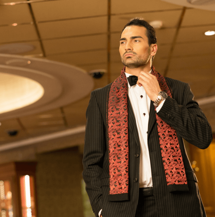 A man in a stylish tuxedo with a red patterned scarf, exuding confidence in a luxurious setting.