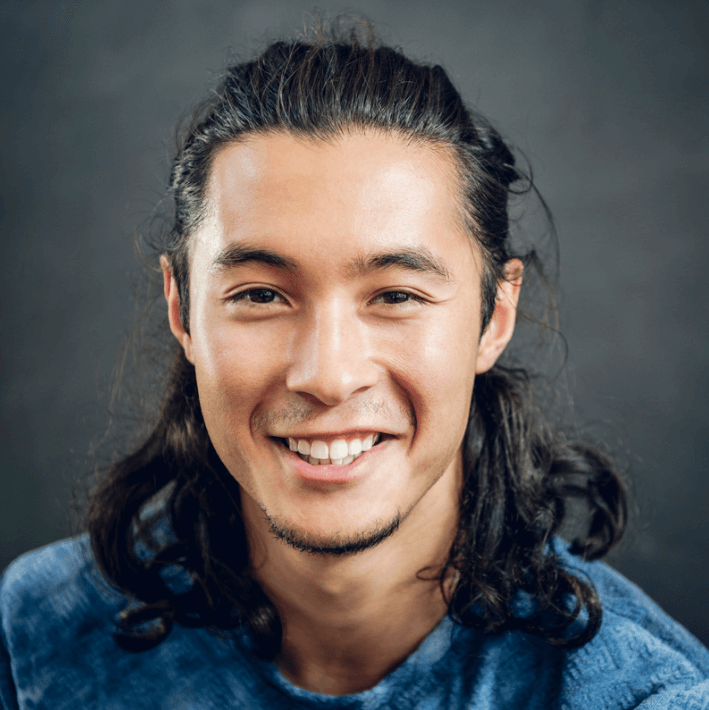 Smiling man with long hair wearing a blue shirt, showcasing a confident and approachable demeanor.