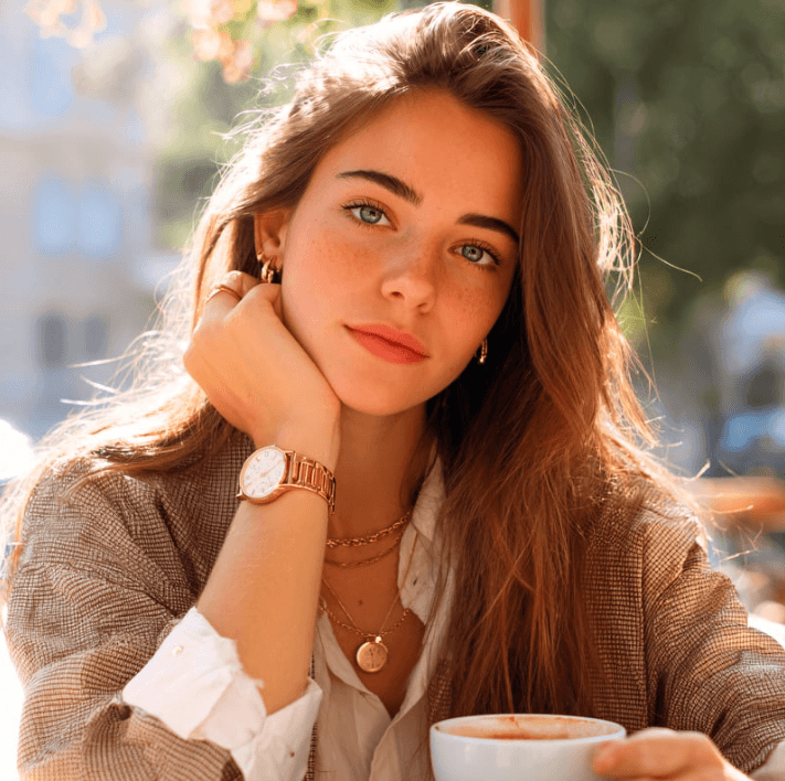Young woman enjoying coffee in a sunlit café, wearing a stylish outfit and jewelry.